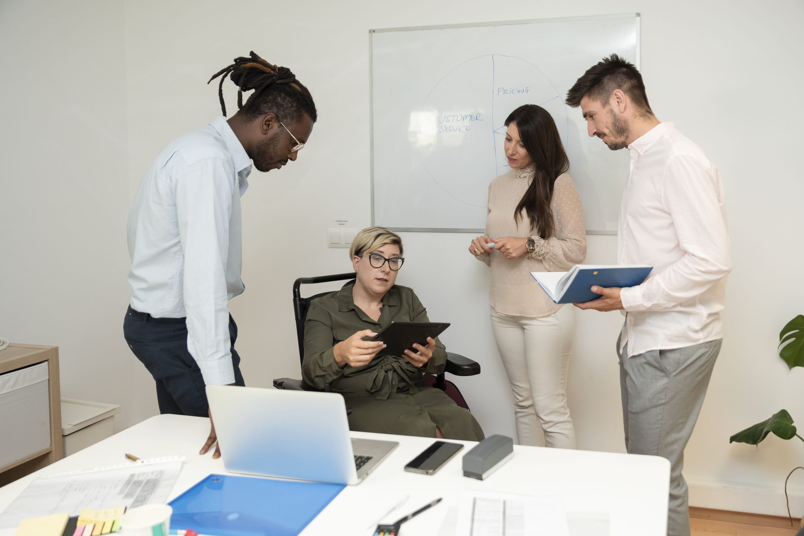 Successful businesswoman in wheelchair meets with her team analyses data on digital tablet