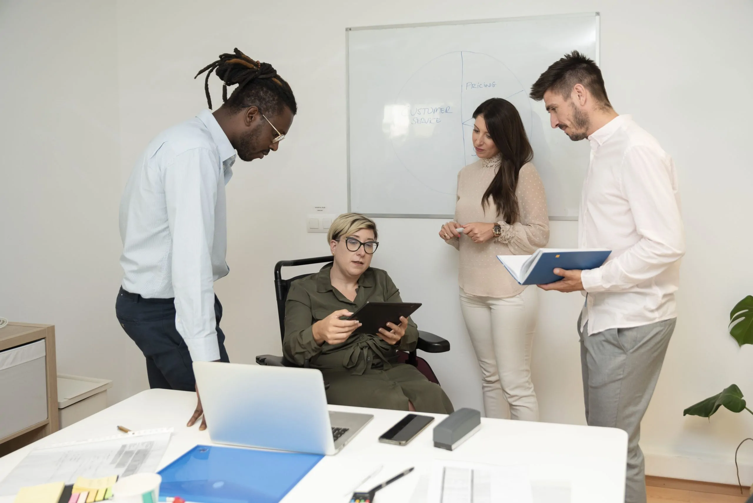 Successful businesswoman in wheelchair meets with her team analyses data on digital tablet