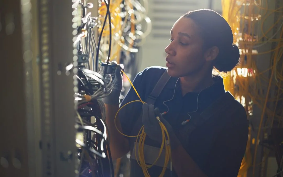 Engineer is working on wiring network cables in server room filled with equipment and devices, focused on completing task efficiently